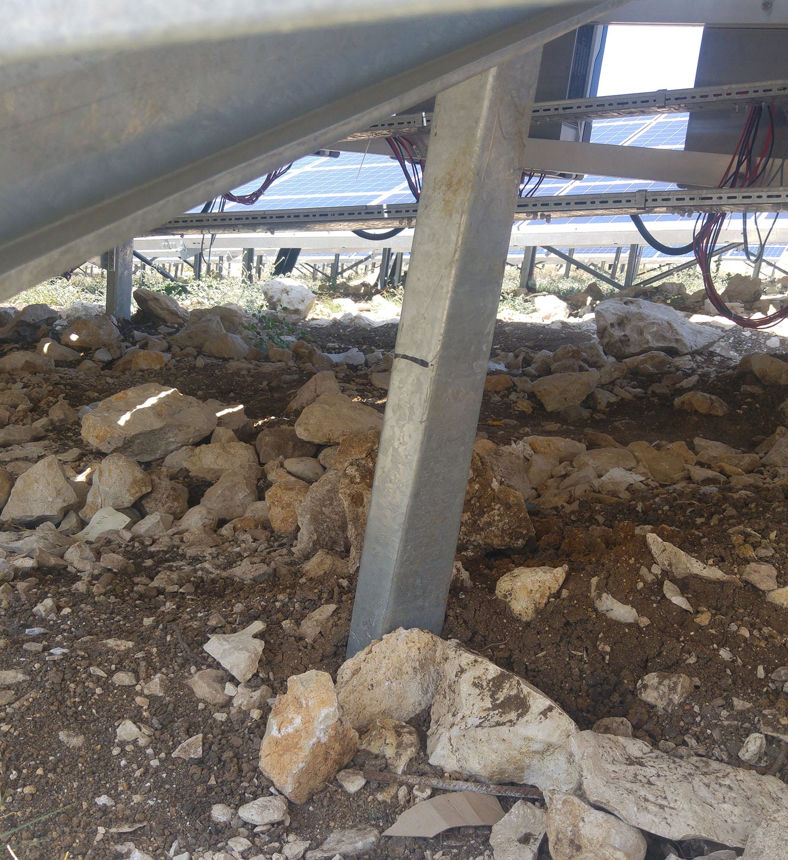 View from beneath a solar array showing a tilted mounting post in rocky ground