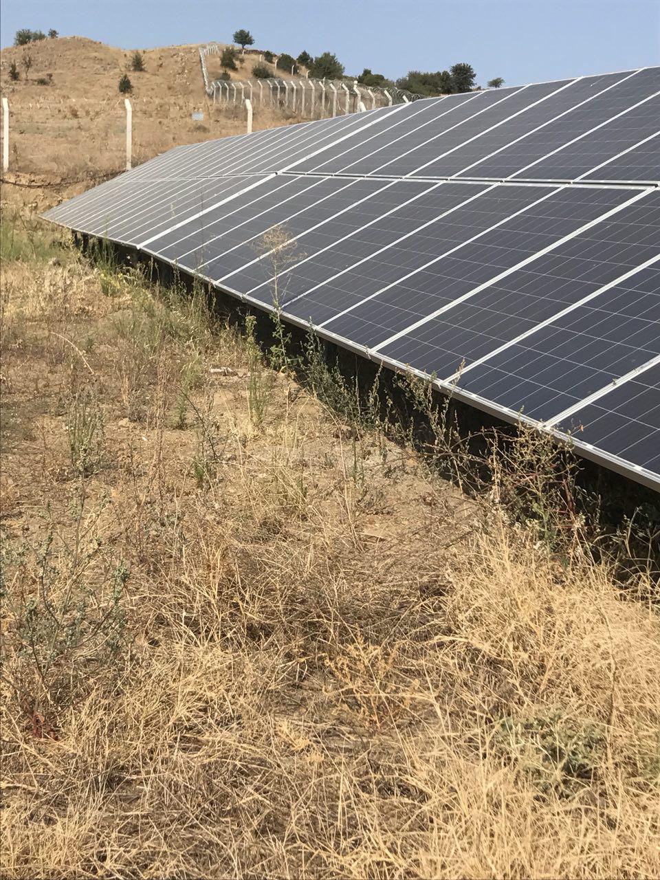 Solar array installed on sloped ground with dry grass and a wire fence in the foreground