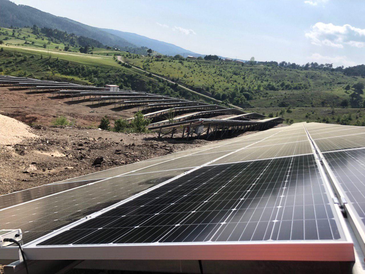 Ground-mounted solar array on sloped, green hillside terrain