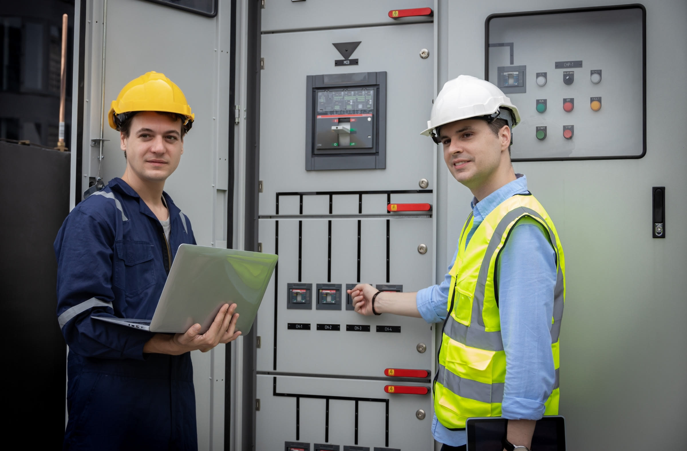 Two engineers with a laptop checking an electrical switchgear panel