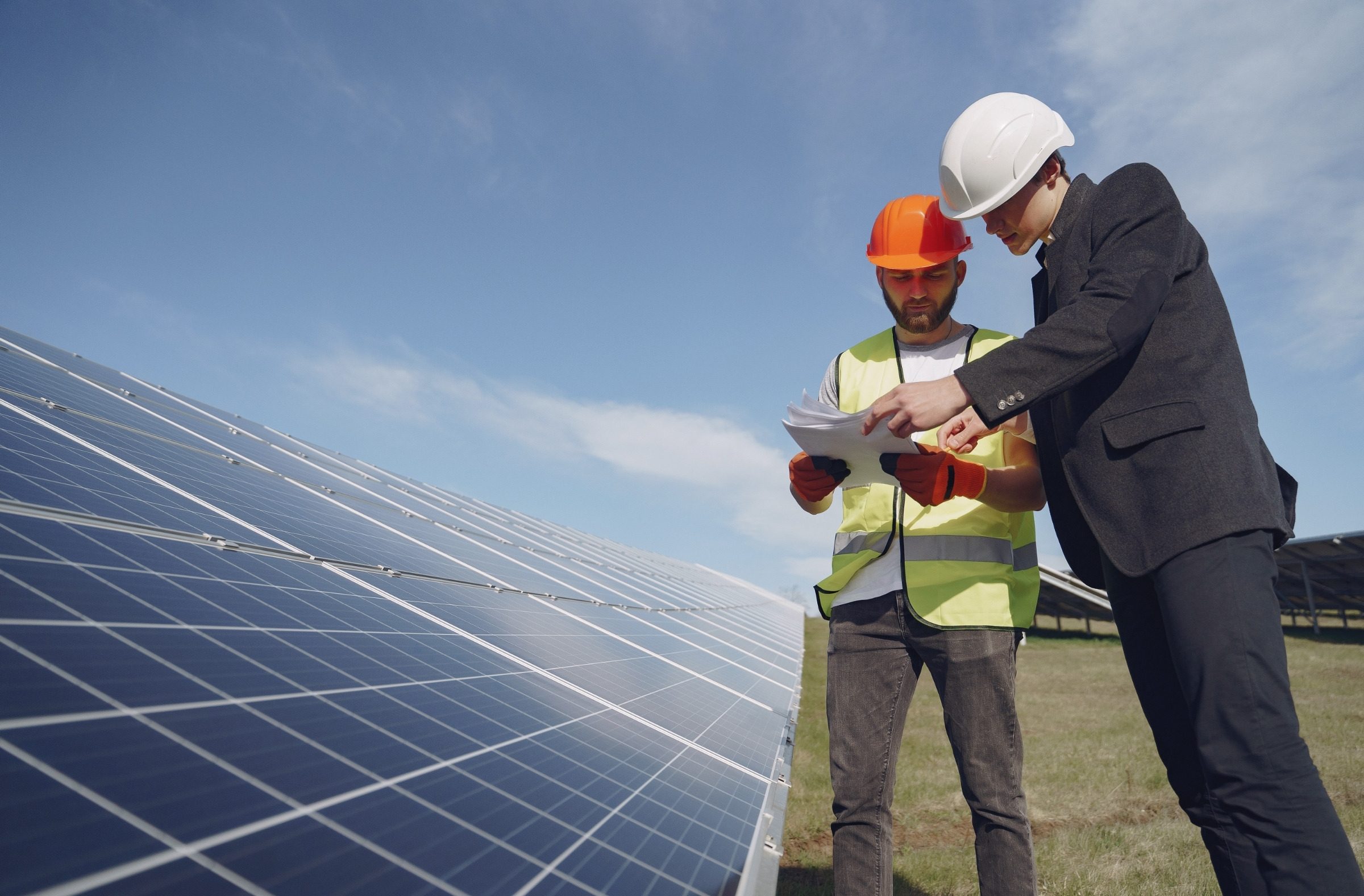 Güneş santralinde panel sırasının yanında birlikte evrak inceleyen iki kişi