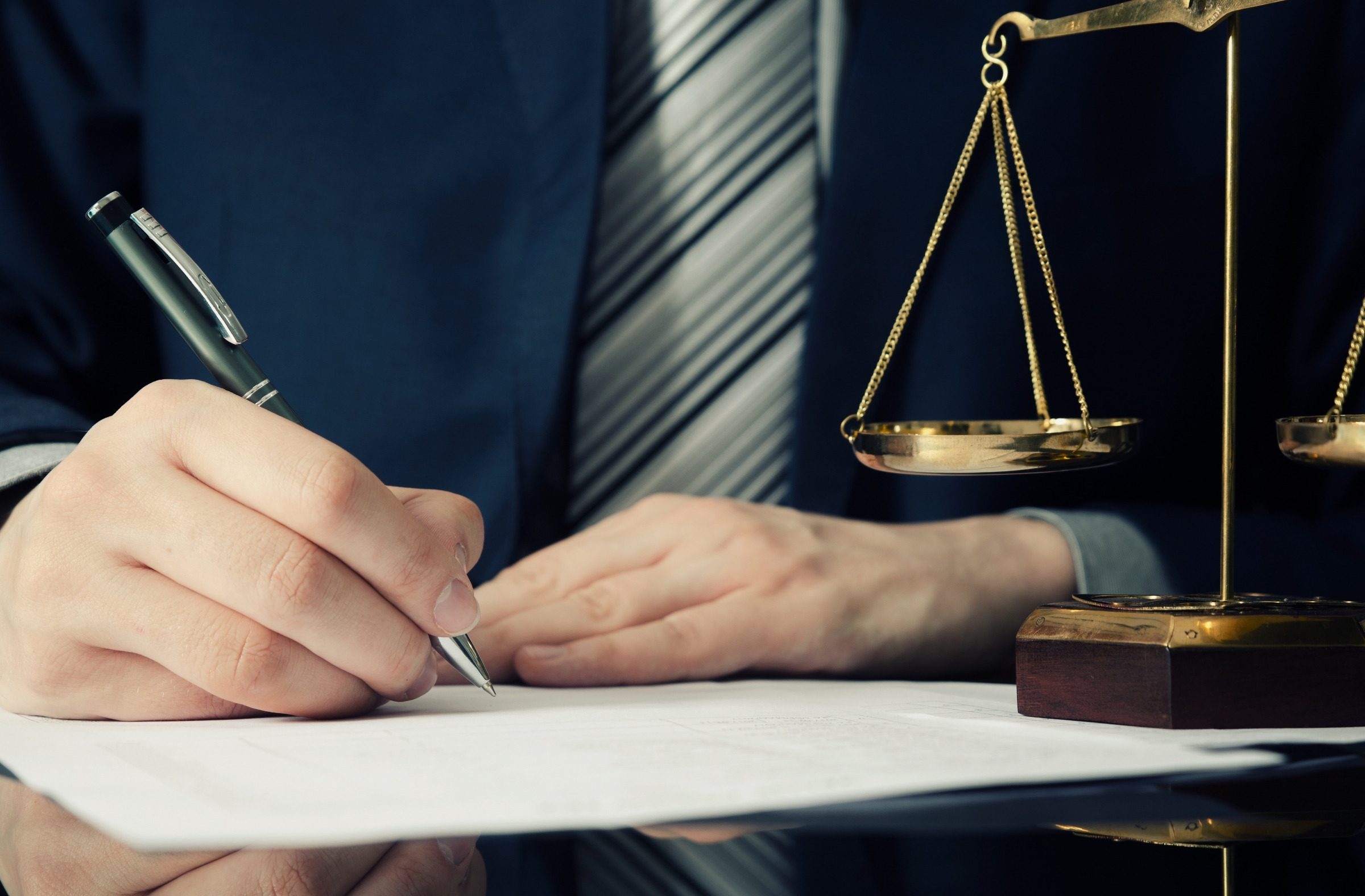A hand signing a document beside a pair of scales