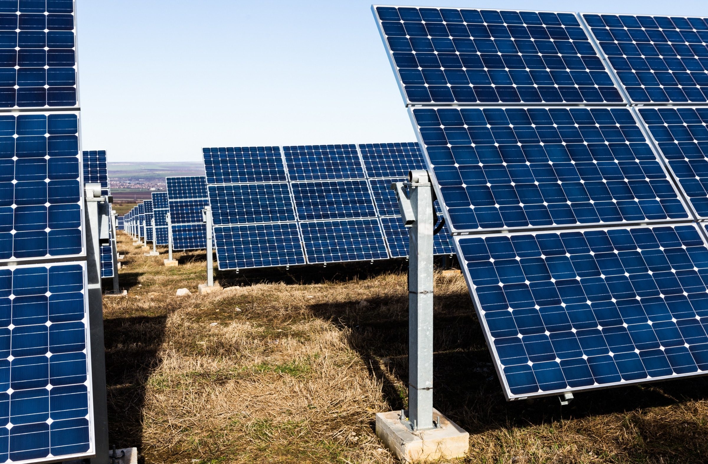 Ground-mount solar module rows on steel piles across a dry field